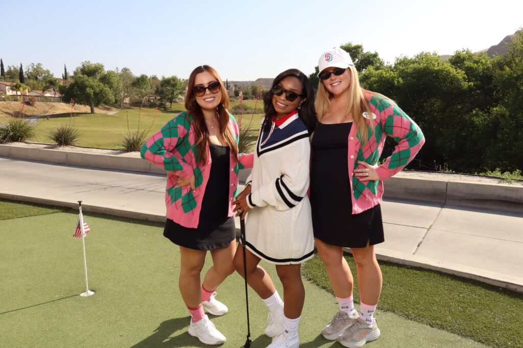 Three guests posing together at an outdoor golf event