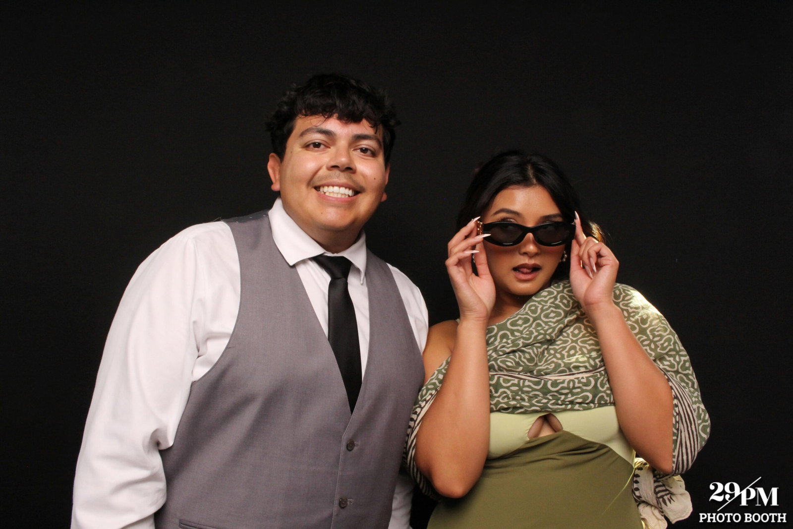 Two wedding guests posing at a 29PM photo booth against a black backdrop