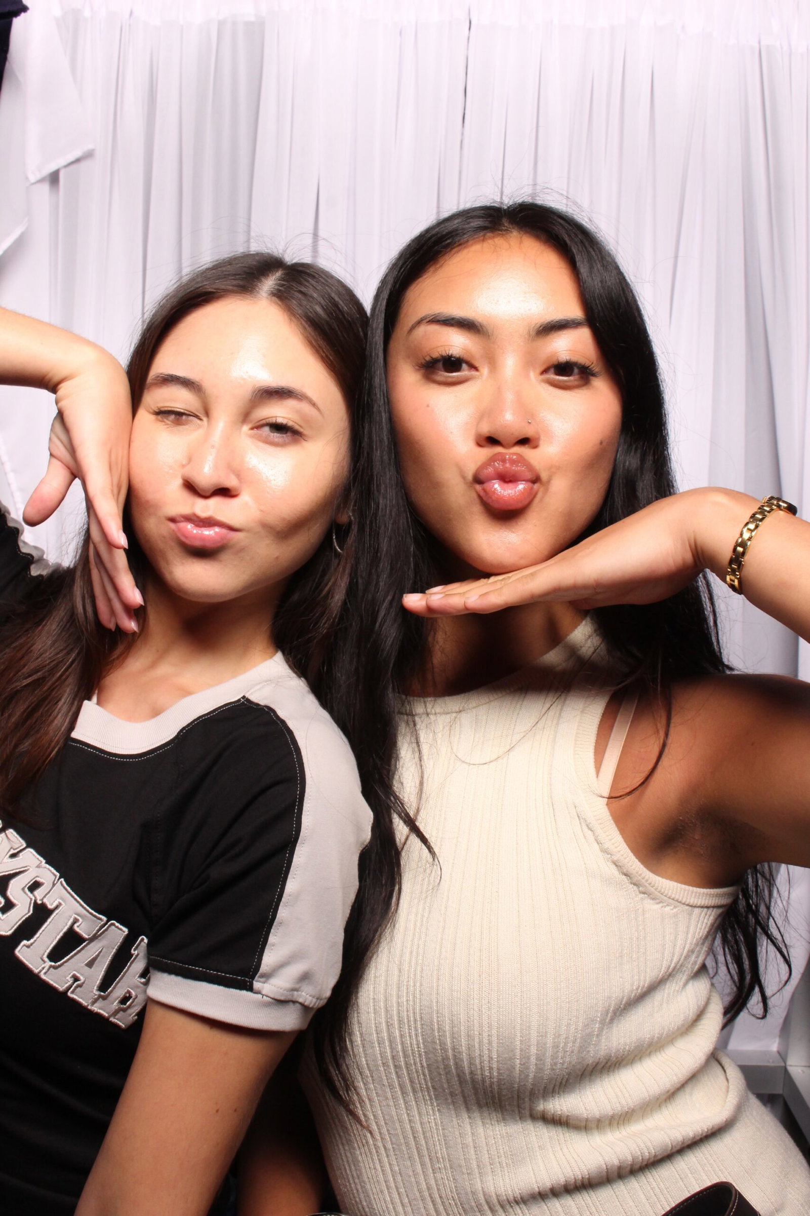 Two friends posing inside a 29PM classic sit-down photo booth with white curtains