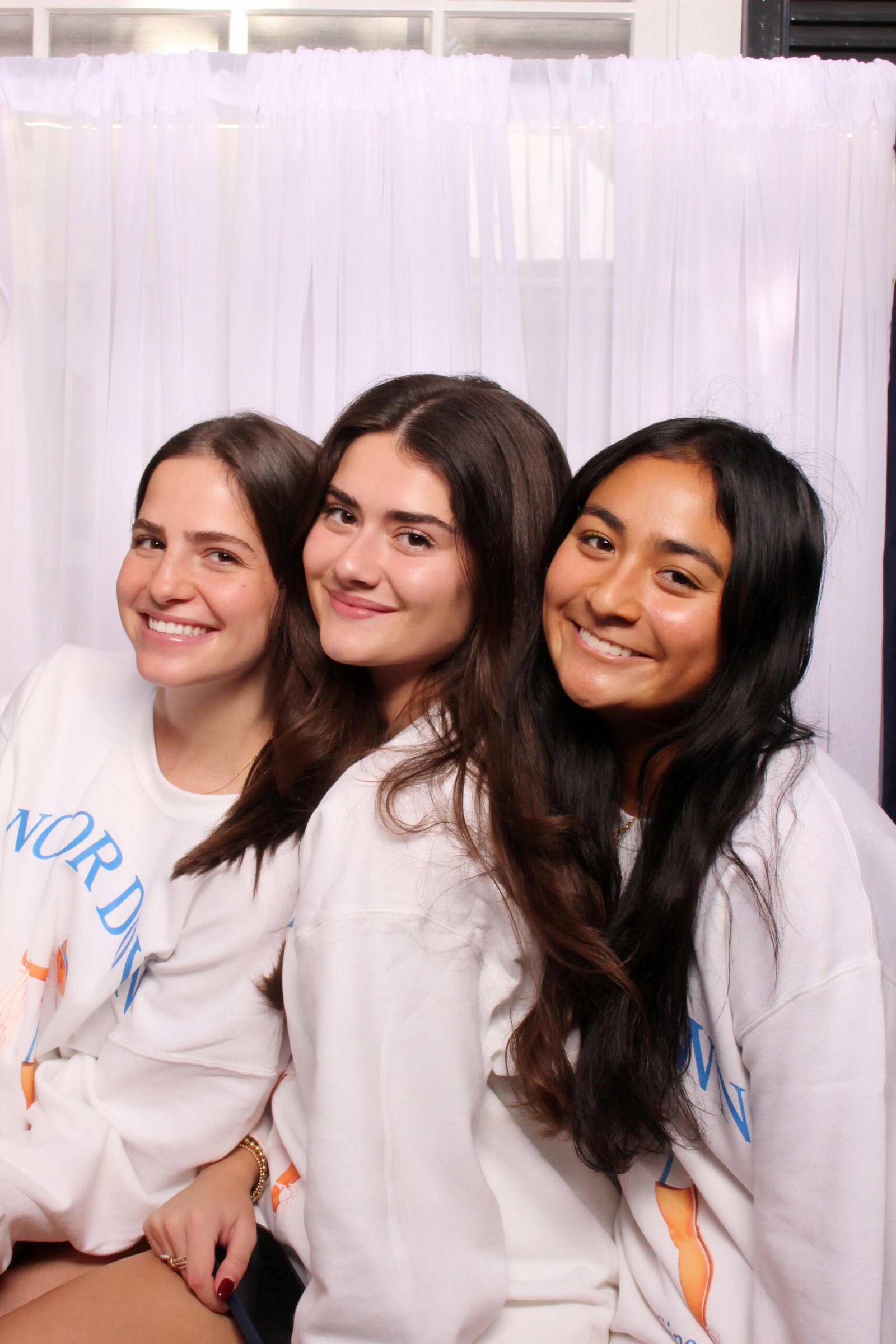 Three friends posing inside a 29PM classic sit-down photo booth with white curtains