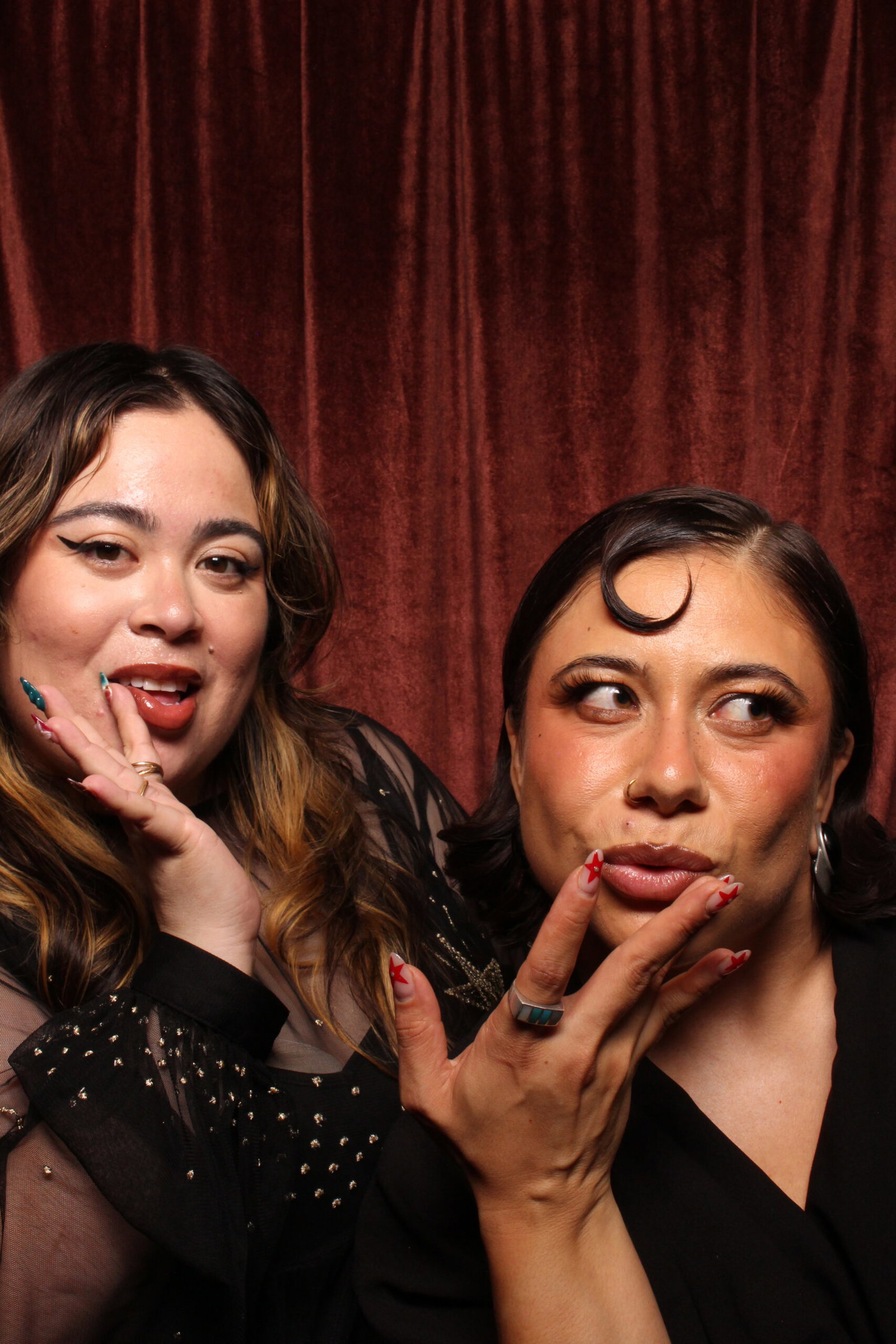 Two friends posing in a 29PM classic sit-down photo booth with a red velvet backdrop