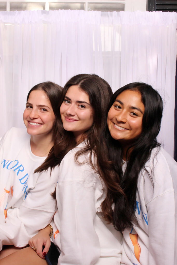 Three friends posing in a 29PM photo booth with a white drape backdrop