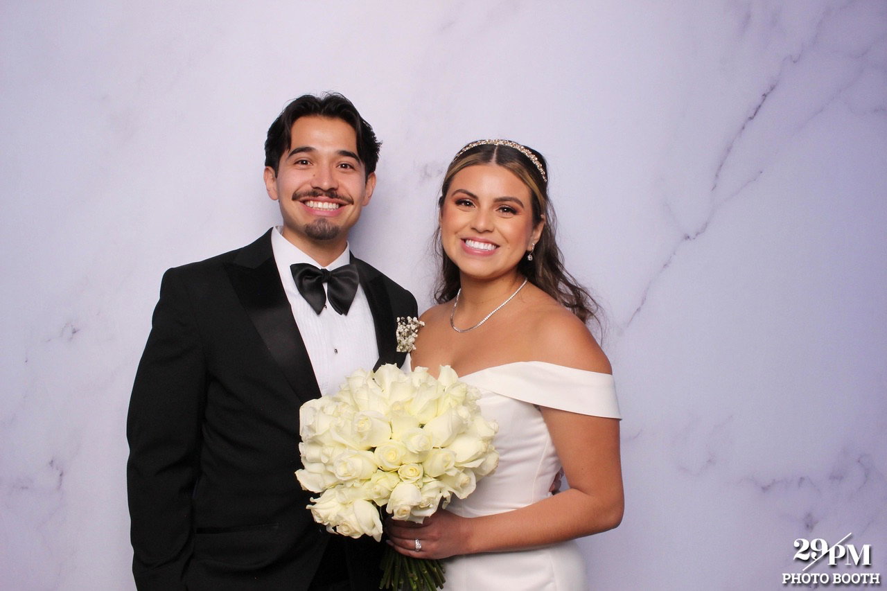 Newlywed couple posing with a white rose bouquet at their wedding photo booth