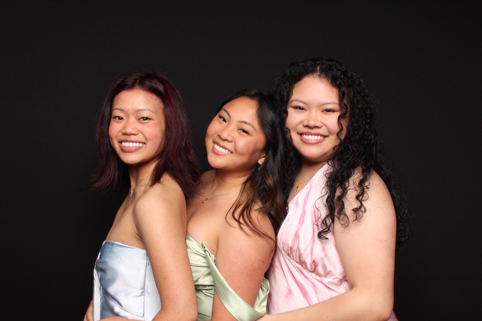 Three friends smiling together against a black backdrop in the 29PM Glam Booth